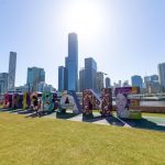Brisbane sign in park framed by modern towers under bright blue sky