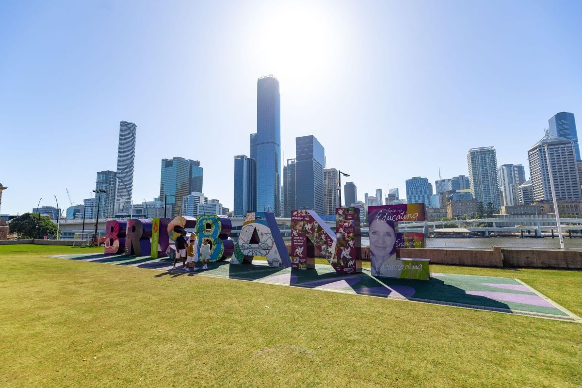Brisbane sign in park framed by modern towers under bright blue sky